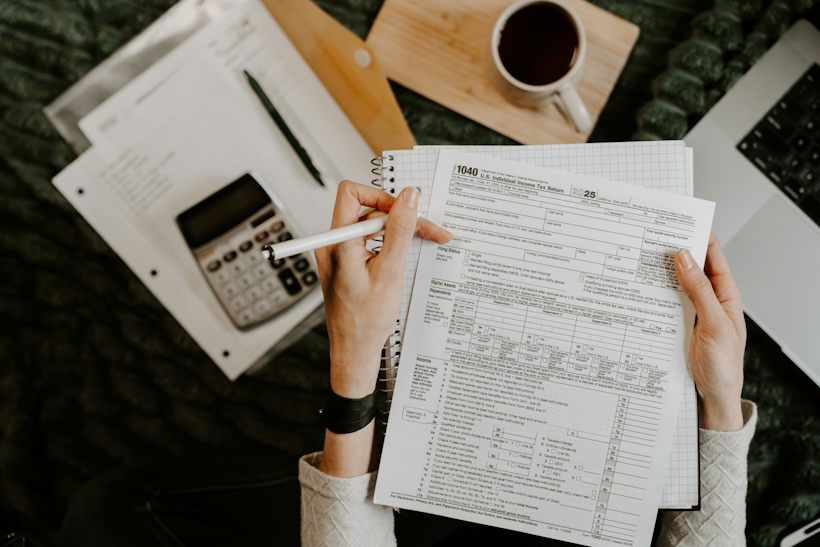 Hands reviewing financial documents beside a calculator and laptop